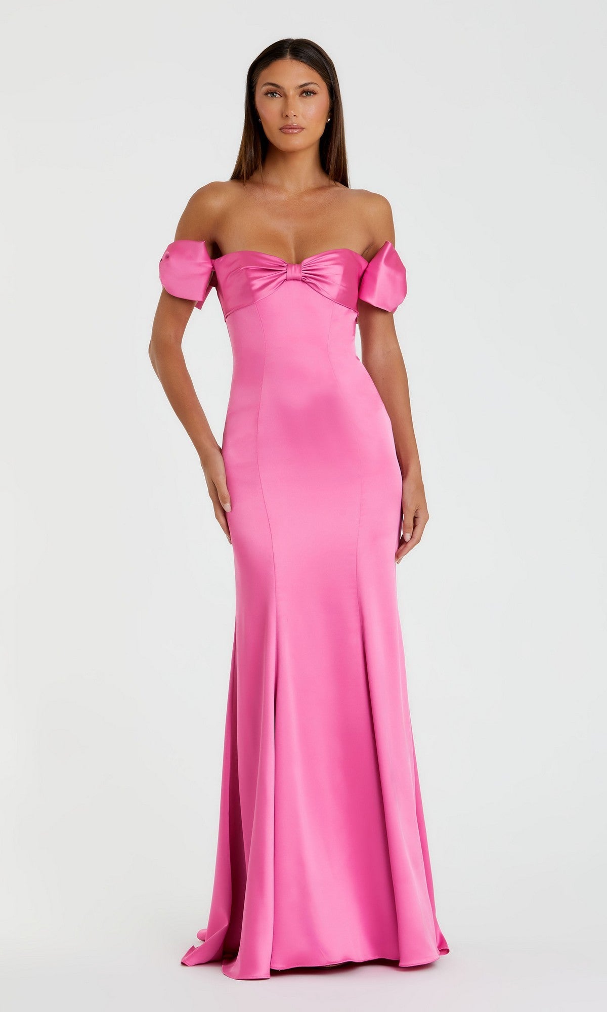 A woman in the Mac Duggal 68875 long formal dress—pink satin, off-the-shoulder, with short puffed sleeves and a knotted bow at the bust—stands against a plain light background.